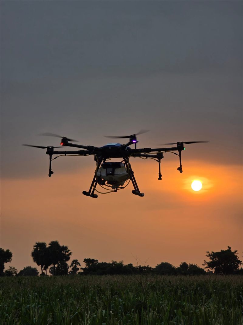 Agricultural spray drone over a field at sunset